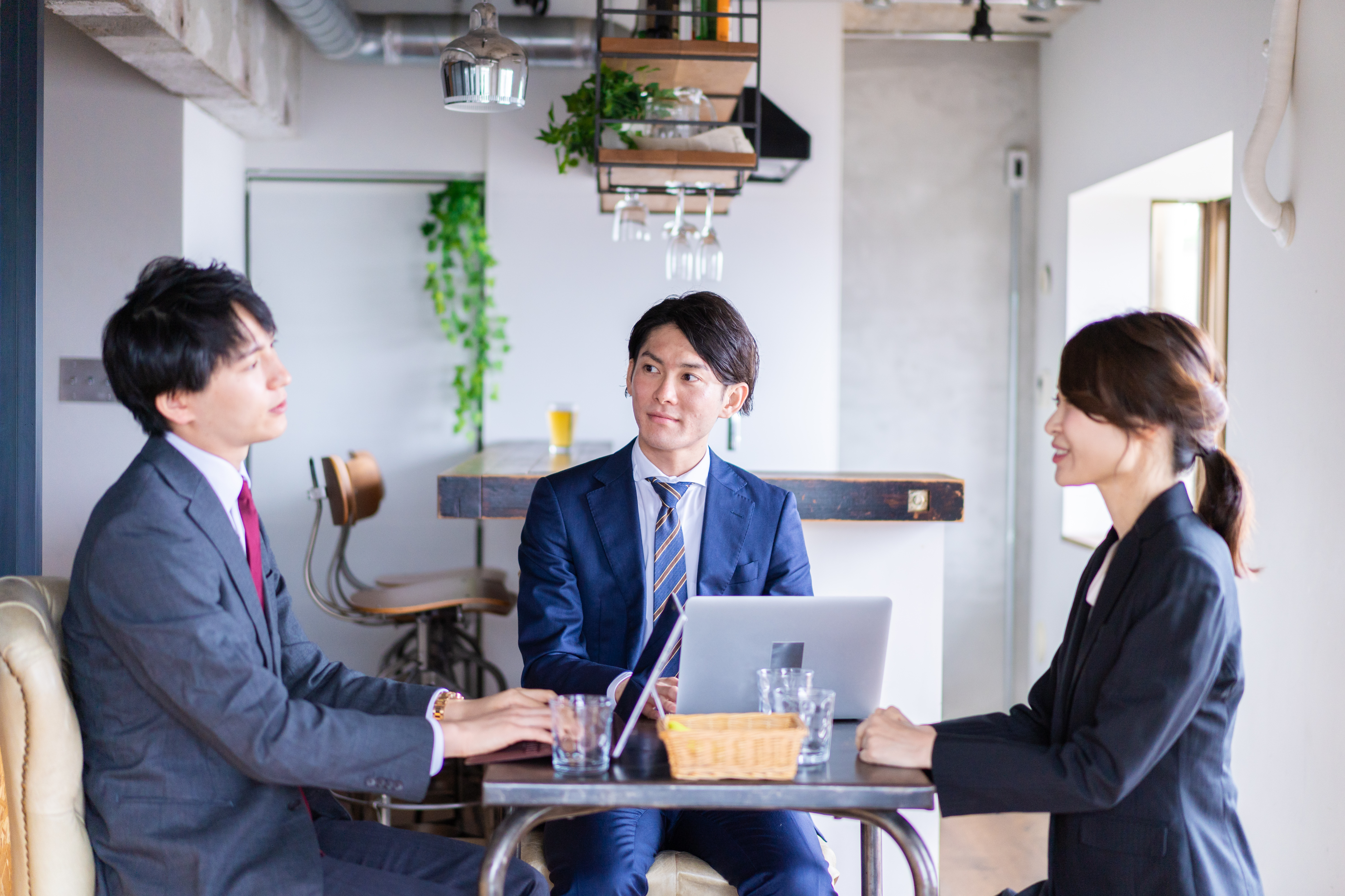 カフェでパソコンを広げながら話をするビジネスパーソン3人