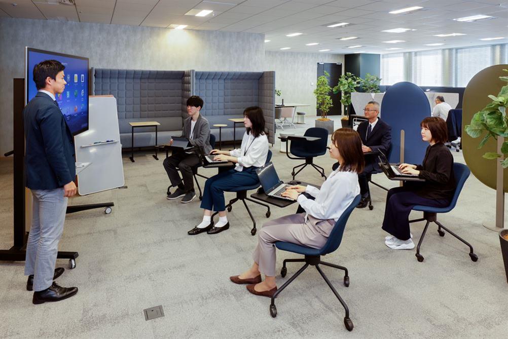 デスクと一体型の椅子を使ってオフィスで研修を受ける人たち